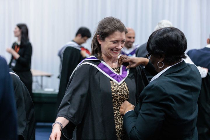 A smiling female student is fitted for her MPhil gown ahead of gradution.